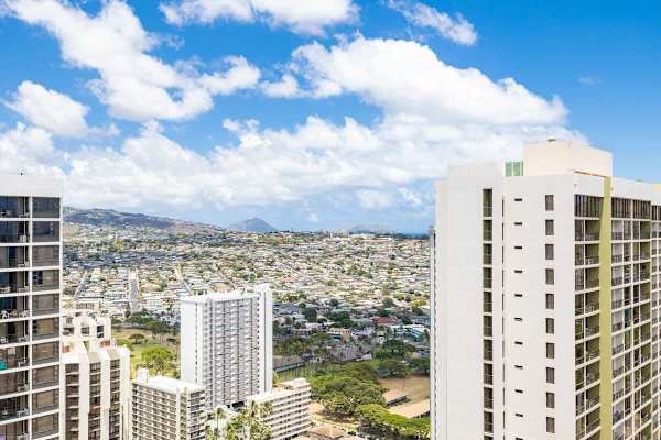 Cityscape view from a high-rise building with a clear blue sky and distant mountains.