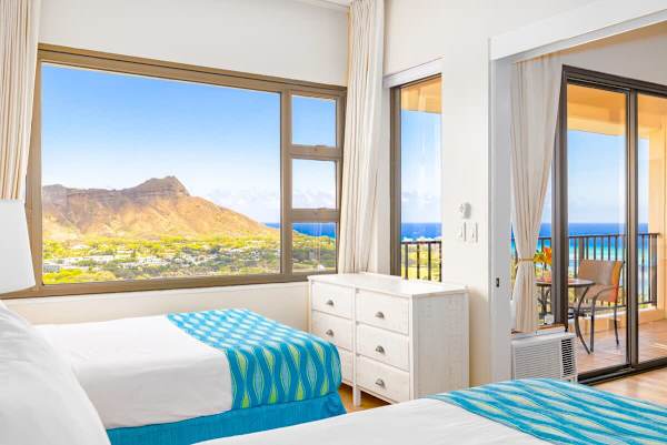 Bright bedroom with ocean and mountain views and access to a balcony seating area