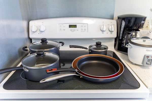 Fully equipped kitchen stove with pots, pans, coffee maker, and rice cooker for convenient meal preparation.