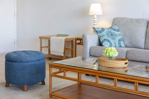 Cozy living area featuring a glass-top rattan coffee table and a blue upholstered ottoman.