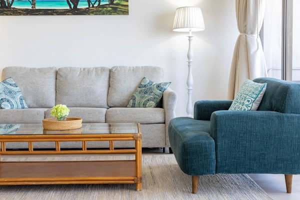 Living room with a beige sofa, teal armchair, and natural wood coffee table in a bright setting
