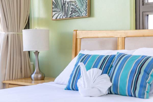 A cozy bedroom corner featuring a wooden headboard, striped blue pillows, and a bedside lamp.