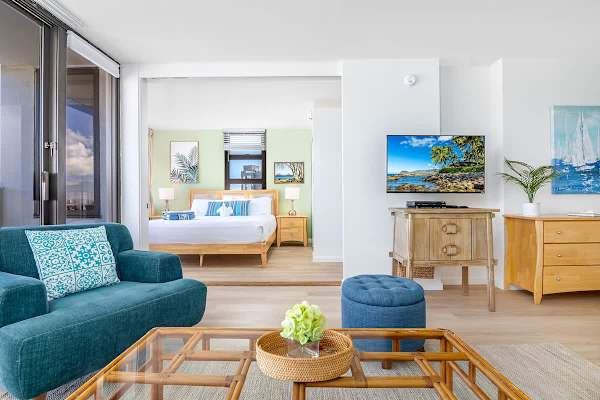 Bright living area with teal sofa and a view into the bedroom featuring coastal decor.