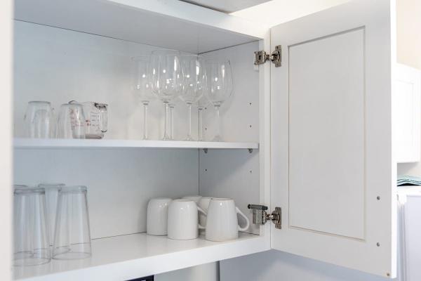 Open kitchen cabinet with a selection of glassware including wine glasses, mugs, and measuring cups.
