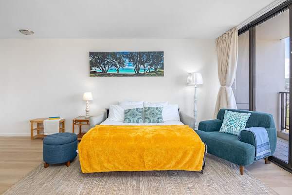 Bright studio with a comfortable bed and seating area next to a large window.