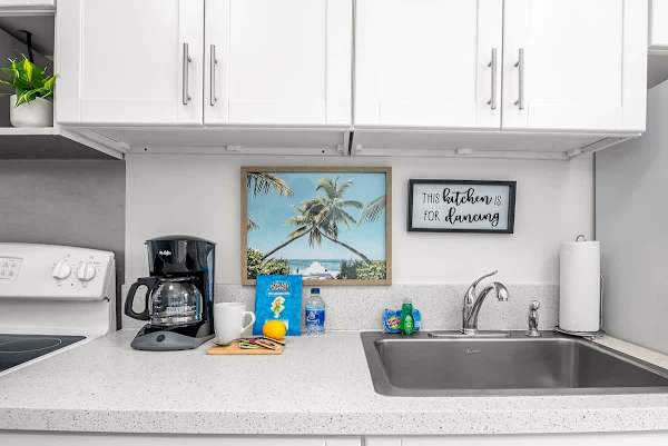 Compact kitchen counter with coffee maker, sink, and tropical wall art for a relaxed atmosphere.