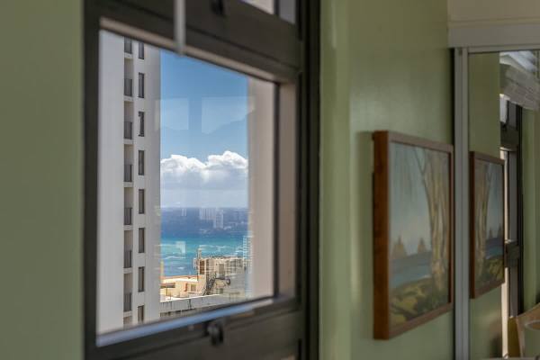 Ocean view framed by city buildings seen through a window in a bright room.