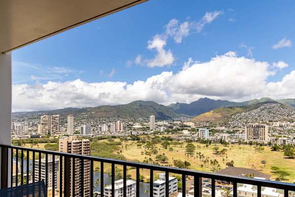 City and mountain views from a high-rise balcony overlooking a green park area.