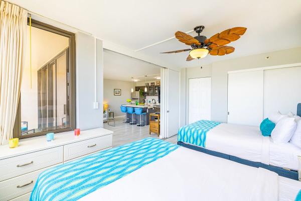 bright bedroom with two beds and a tropical ceiling fan overlooking the kitchen area