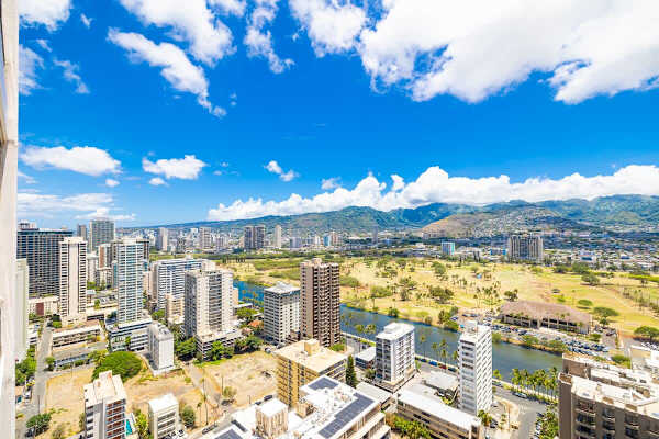 Cityscape view with a golf course and mountains under a bright blue sky.