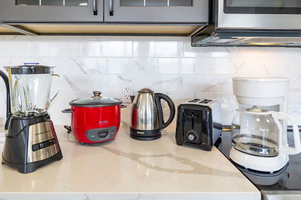 Modern kitchen countertop with essential appliances including a blender, rice cooker, electric kettle, toaster, and coffee maker.