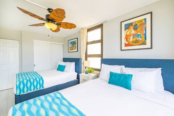 Bright bedroom with two blue-upholstered beds and tropical-themed decor.