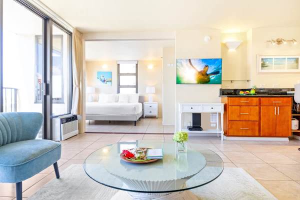 Bright living area with a glass coffee table and a view into the bedroom.