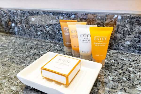 Essential bath toiletries including shampoo, conditioner, body lotion, shower gel, and cleansing bar on a granite countertop.