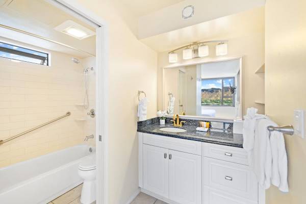 Bright bathroom with granite countertop and a view of the mountains through the bedroom window.