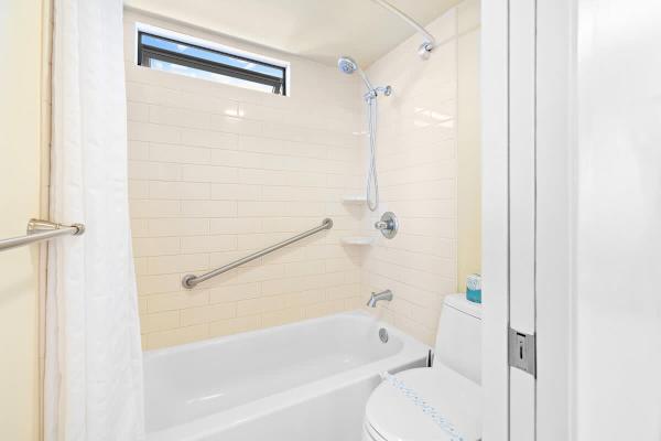 Bright bathroom with a bathtub and shower combination featuring a safety grab bar.