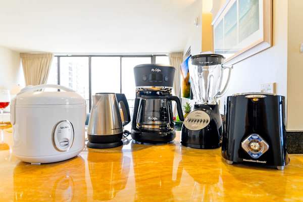 Kitchen countertop featuring a coffee maker, blender, kettle, rice cooker, and toaster with natural light from large windows.