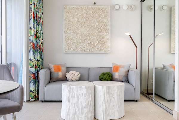 This inviting living space features a gray sofa with decorative throw pillows, two white, textured, cylindrical coffee tables, and a modern floor lamp, all contributing to a stylish and relaxed ambiance.
