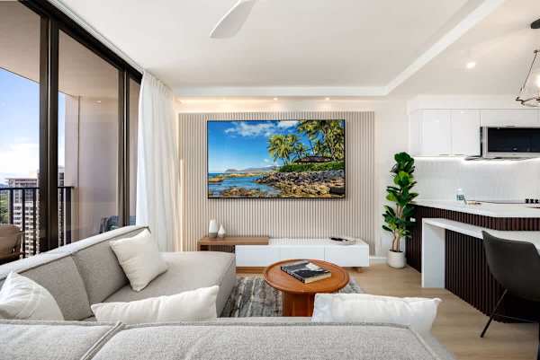 Relax and unwind in your spacious living room, featuring a comfortable sectional sofa, an 85" smart TV for entertainment, and abundant natural light from your private balcony.