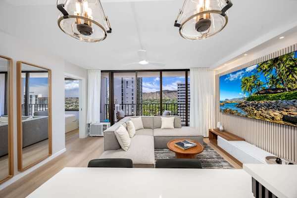 Relax in your comfortable and modern living room, featuring an impressive 85" Smart TV, refreshing Window AC, and stunning views of Diamond Head and the vibrant city for an unforgettable island getaway.