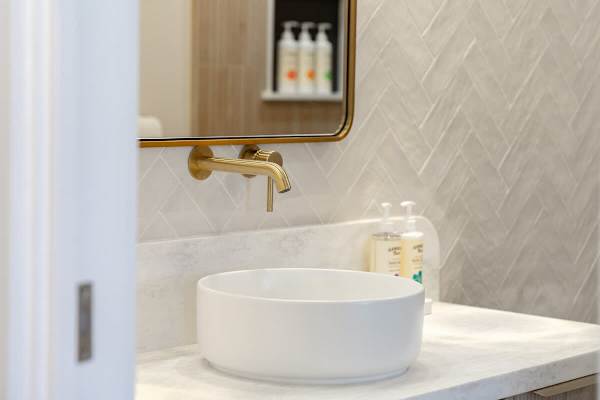Indulge in refined comfort at your spa-inspired vanity, featuring a sleek vessel sink and elegant gold fixtures for a touch of luxury.