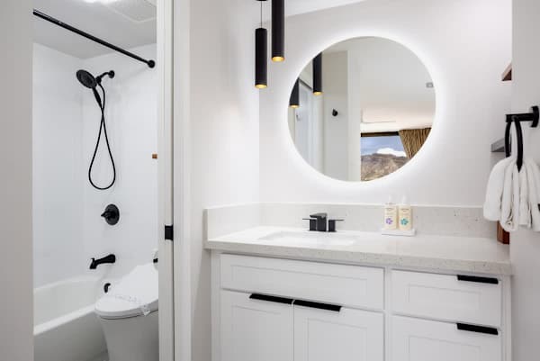 Unwind in our modern bathroom, featuring a vanity with a round backlit mirror and a tub-shower combination for your ultimate comfort!