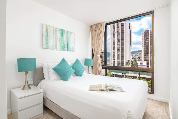 This second bedroom features a full-size bed, vibrant accents, and a large window offering city views, perfect for a relaxing retreat.