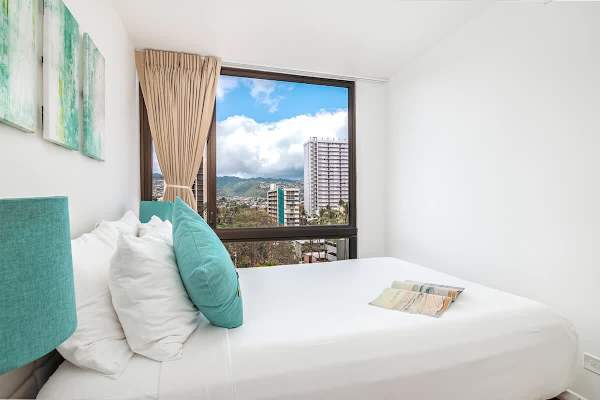 Enjoy peaceful slumber in the second bedroom, featuring a full-size bed and a large window framing picturesque city and mountain views.