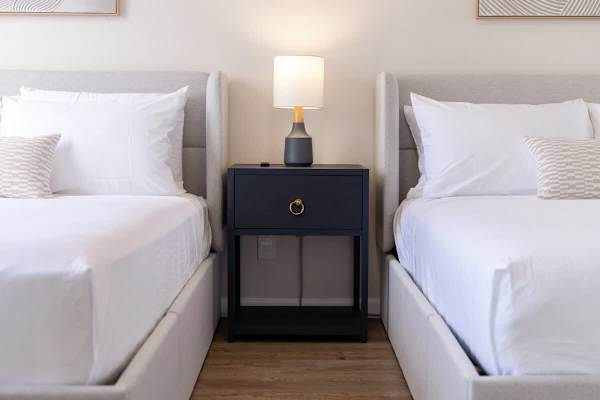 Settle into comfort with two plush beds separated by a stylish nightstand, illuminated by a warm bedside lamp.