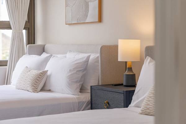 Drift off to sleep in this serene bedroom, featuring a queen and a full-size bed, a stylish nightstand with a warm lamp, and elegant wall art.