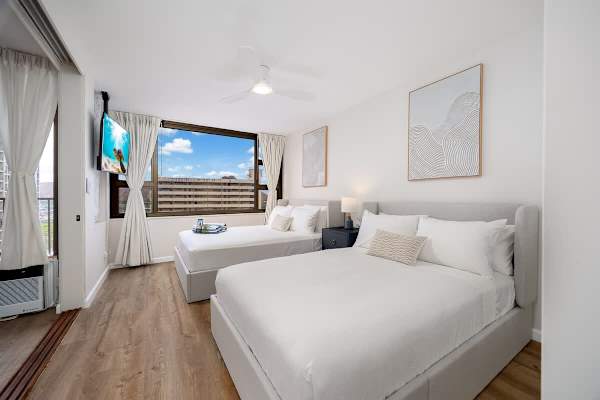 This condo features a cozy bedroom with a queen-size and a full-size bed, plus a window which offers a glimpse of the city.