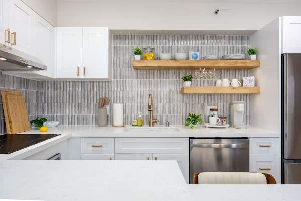 Prepare meals with ease in this well-appointed kitchen, featuring a sleek dishwasher, gold-accented faucet, and open shelving stocked with dinnerware and glasses.