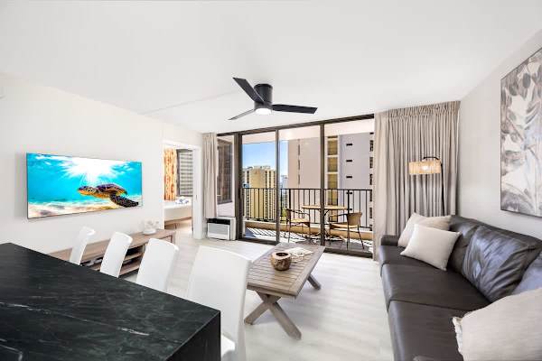 Relax in your bright and airy living room featuring a sofa, a 55" Smart TV visible from the bar seating, and a lovely balcony offering great views!