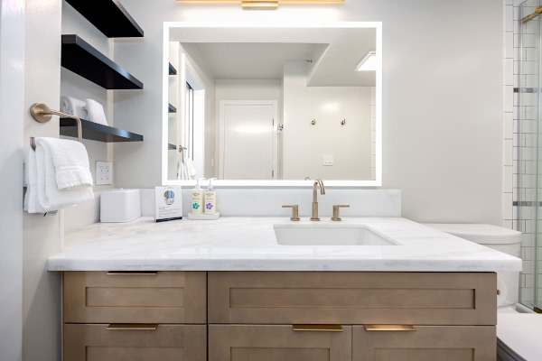 Your modern bathroom features a gorgeous marble vanity with stylish brass fixtures, an illuminated mirror, and convenient shelving stocked with fresh towels and complimentary toiletries for your use!