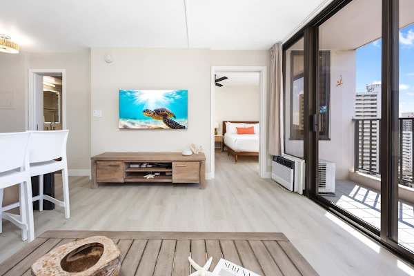 From this angle, you can appreciate the light-filled flow of the apartment, featuring a 55" Smart TV, and easy access to both your private balcony and the cozy bedroom!