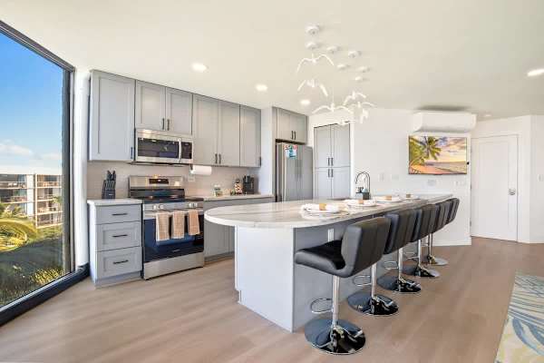 This chic kitchen features sleek gray cabinets, stainless steel appliances, and a curved bar seating area with captivating views through the large window.