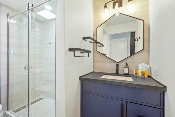 Refresh in this modern, well-lit bathroom featuring a chic navy vanity, hexagonal mirror, and a glass-enclosed shower with stylish tile work.