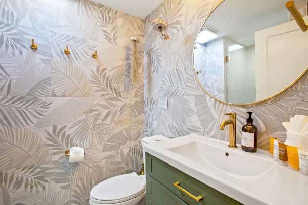 Indulge in this luxuriously appointed bathroom featuring stunning tropical leaf-patterned tiles, a modern green vanity, and elegant gold fixtures for a spa-like experience.