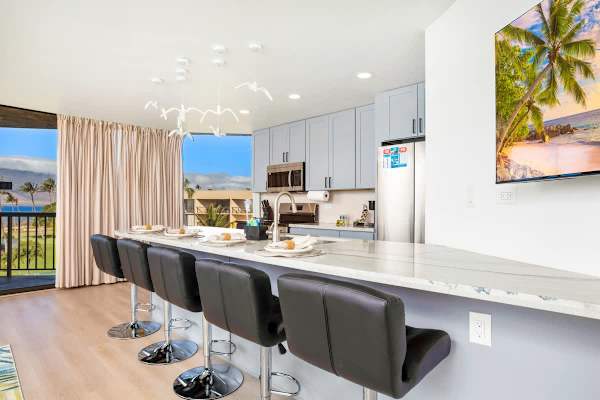 Dine with a stunning ocean view at the kitchen island, featuring modern black bar stools, a marble countertop, and unique seagull light fixtures.