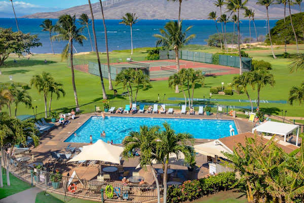 Discover the expansive resort grounds featuring a sparkling pool and tennis courts, all set against the backdrop of the blue Pacific and the distant, majestic West Maui mountains.