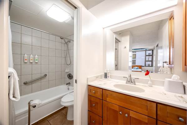 Freshen up in this sparkling clean bathroom, featuring a well-lit vanity with ample counter space, a bathtub with a shower, and complimentary toiletries for your convenience.