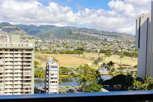 City and mountain views from a high-rise balcony with a nearby park and water feature.