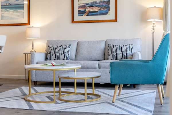 Modern living room with a gray sofa, patterned cushions, and a teal accent chair centered around nested marble-top coffee tables.