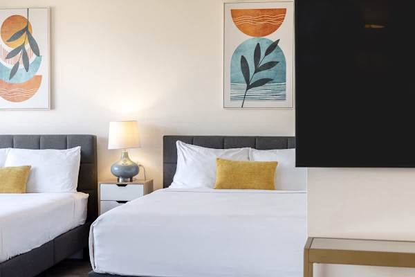 Modern bedroom with two queen beds, colorful artwork, and a flat-screen television.