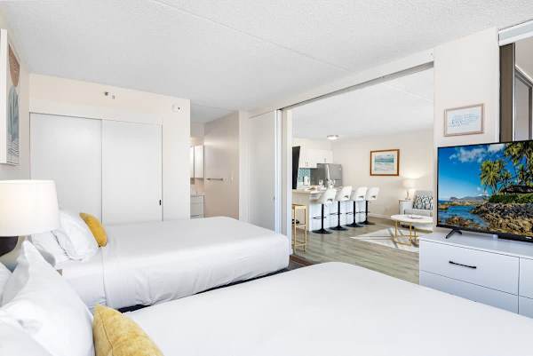 Bright bedroom with two beds and a view into the modern kitchen and living area.
