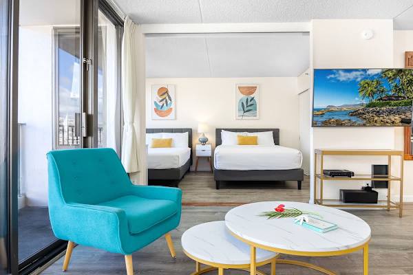 Bright living area with a turquoise armchair and two queen beds in the background