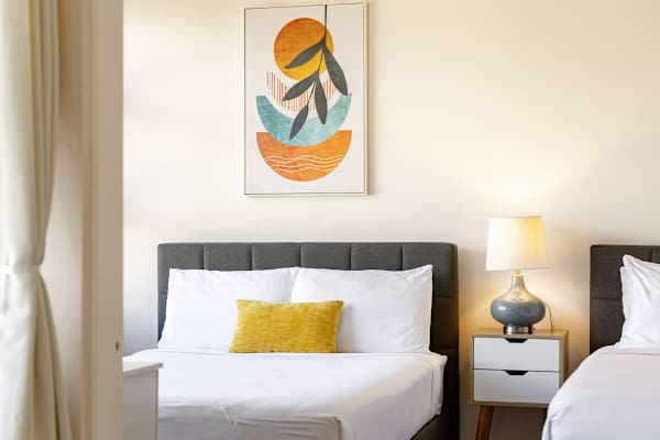Modern bedroom with two beds, a bedside table, and abstract wall art.
