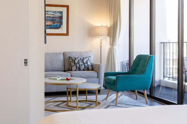 Modern living area with a teal accent chair and natural light from floor-to-ceiling windows.