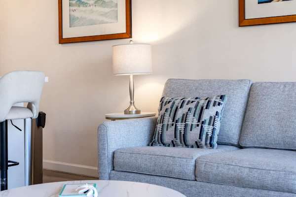 Modern living area with a comfortable gray sofa and decorative pillow next to a lit table lamp.