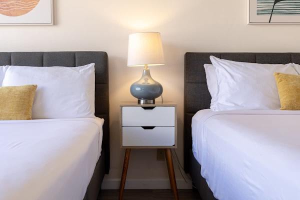 Two modern beds with a shared nightstand and lamp create a cozy sleeping area.
